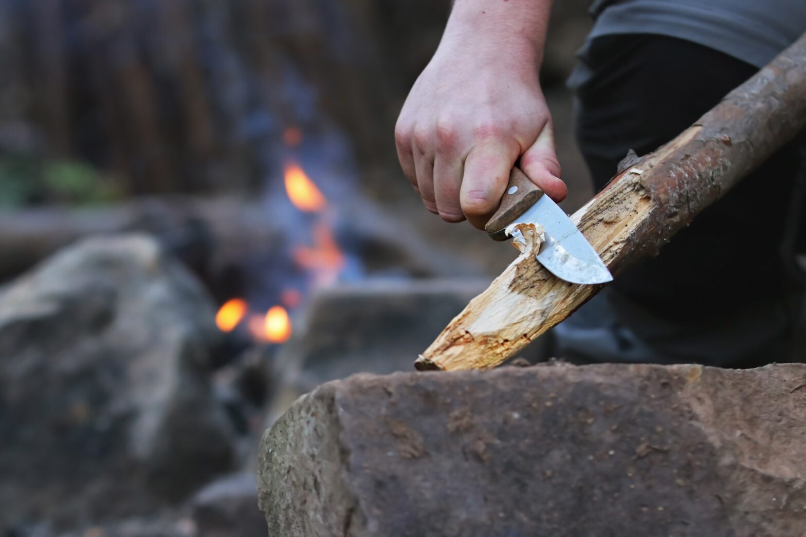man using hunting knife to carve a stick